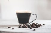 a cup of black coffee with coffee beans scattered around it