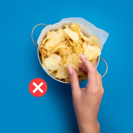 A hand picking crisps with a red cross alongside